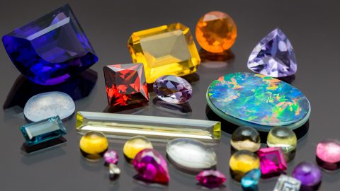 An assortment of different gemstones in many shapes and sizes and colours scattered on a black perspex background
