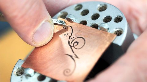 A copper sheet with a hand drawn calligraphic letter N being engraved using a graver