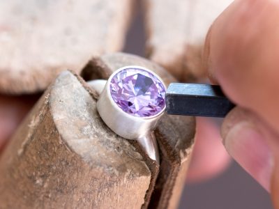 A large round faceted lavender cubic zirconia being set in a silver ring with a pusher tool