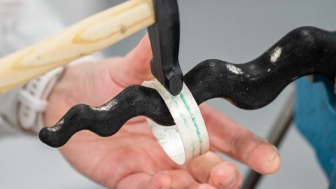 a silver bangle being hammered on an anticlastic raising stake against a plain grey background