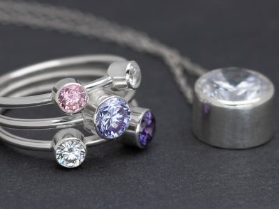 Silver ring with a number of round faceted stones and a silver setting also with a faceted stone on a slate background