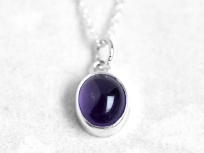 Silver pendant with amethyst cabochon gemstone on a silver chain against a stone background
